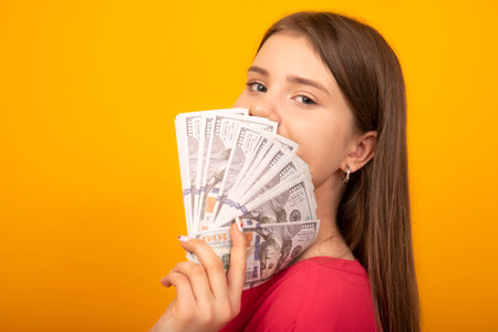 Young woman holds wad US dollars li fan on a bright yellow yellow background. copy space