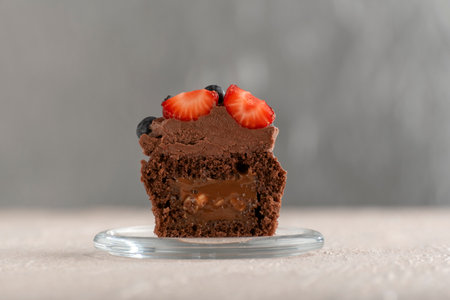 Delicious brown cupcake decorated with chocolate cream and berries on glass plate. Fresh muffins with butter glazeの写真素材