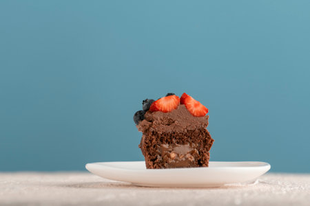 Chocolate brown cupcake decorated with chocolate cream and berries on glass plate. Muffins with butter glaze. blue background. high quality photoの写真素材