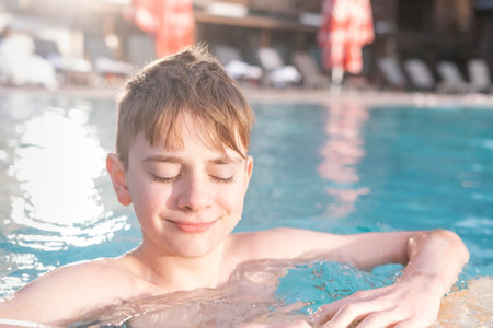 Cute boy guy teen teenager with brown hair in outdoor pool frowning off from the bright sunの写真素材