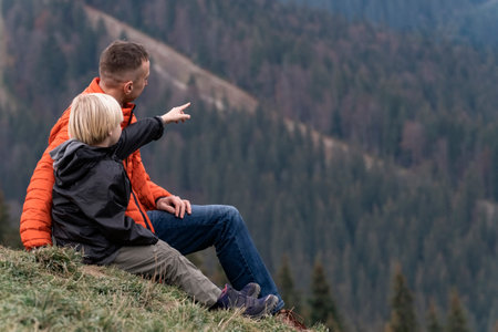 Young father and son child boy sit on slope and look at the mountains. Family hike with children in autumnの写真素材