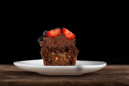 Fresh chocolate muffin with berries.Half chocolate cupcake with filling in cut on wooden surface on black background.の写真素材