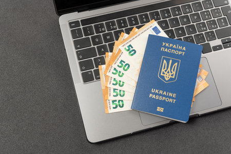 Passport of citizen of Ukraine and euro banknotes on laptop on gray background. Concept of remote work, study, travel and immigration for Ukrainiansの写真素材