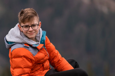 Portrait of teenage boy with brown hair in glasses and sports autumn jacket. Guy looks into the camera and smilesの写真素材