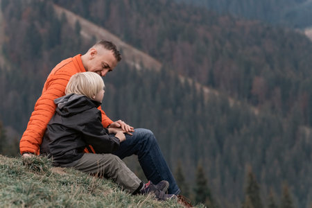 Father and his son sit on the slope and look at the mountains. Family trekking with children in the forest.の写真素材