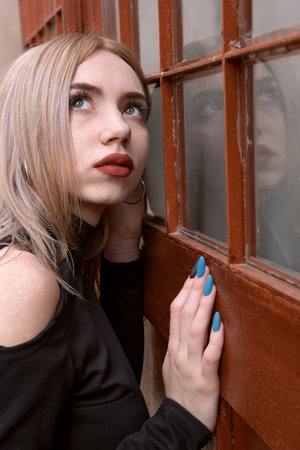 Portrait close up of young blonde girl with red lips and blue manicure near retro door. vertical frameの写真素材