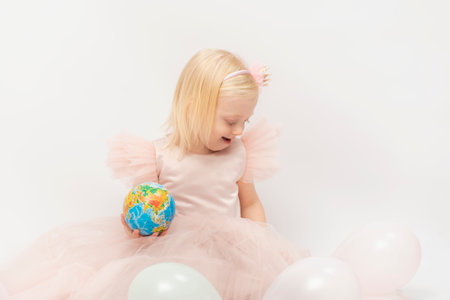 Cute little girl in lush dresslooks at small globe hands. White balloons , on white background. children's holiday.の写真素材