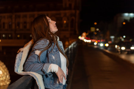 Portrait of young brunette woman on bridge on night city backdrop. Stylish girl on night city streetの写真素材