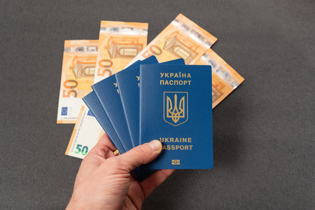Four Ukrainian passports in men's hand, cash euros on background. Obtaining and exchanging foreign...