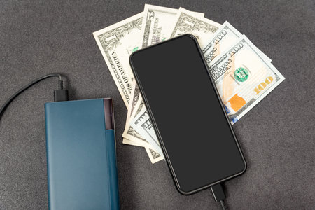 Mobile phone, power bank and dollars cash money on gray background. Modern technologies save money conceptの写真素材