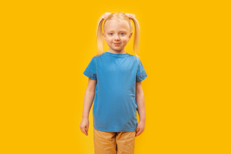 Portrait of blonde girl with two ponytails in blue T-shirt on yellow background. Preschool child 5-6 years oldの写真素材