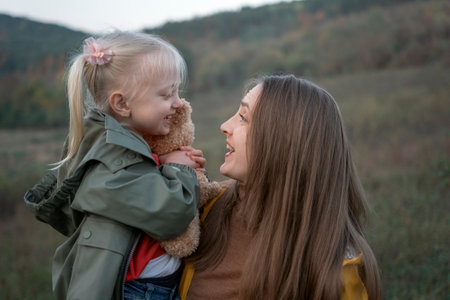 Young mother with daughter in arms laughs and has fun in nature on autumn day. Portrait of girl with child outdoors.の写真素材