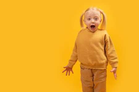 Surprised or frightened girl with her mouth open looks. Preschool girl on yellow background. copy spaceの写真素材