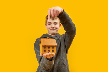 Boy holds wooden house in the palm of his hand and points his finger at it. Buying house. Rental or mortgage of real estateの写真素材