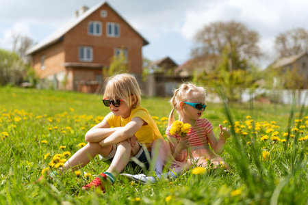 Blond girl and boy in sunglasses sit in grass on meadow. Children rest in dandelion field. happy child summer outdoorsの写真素材