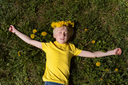 Portrait of blond little boy in yellow t-shirt lying on the grass with close eyes. Child sleeps on...