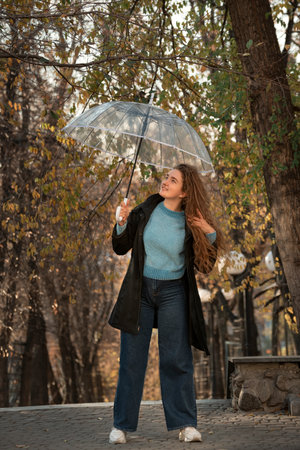 Beautiful girl in black cloak smiles and adjusts her lush hair. Student walks with transparent...