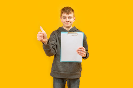 European teenager boy holds blank white sheets of paper and shows thumbs up. Space for text and advertising. copy spaceの写真素材