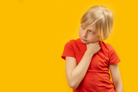 Studio photo of caucasian blonde boy in red T-shirt on yellow background. Brooding child looks to the side. copy spaceの写真素材