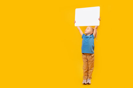 Little girl blank blanc white sheet of paper high above her head. Child with an empty white board. copy spaceの写真素材