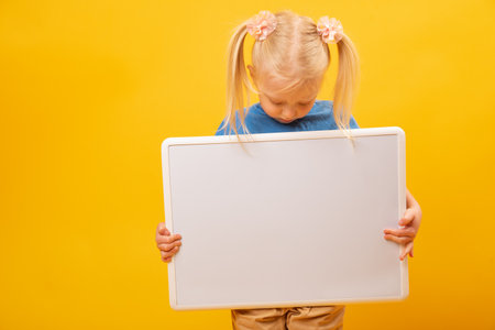 Little blonde girl holds white blank board. copy space mockup. Preschool education, courses for...