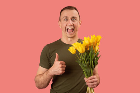 Man holding bouquet of yellow tulip flowers shows thumbs up and screaming with open mouth. Isolated...