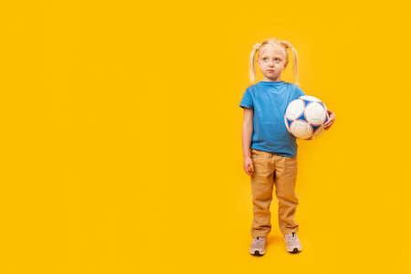 Full-length portrait of young girl with soccer ball. yellow background. Girl love football. copy space mockup.の写真素材