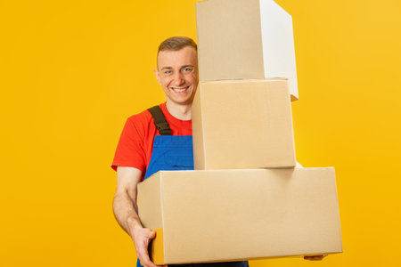Portrait of young man courier with parcels. Loader holds three large boxes and smiles . Copy space,...