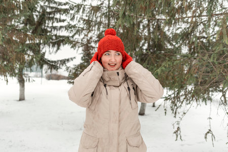 Laughing attractive girl in red knitted mittens and hat in winter forest. Woman in comfortable...