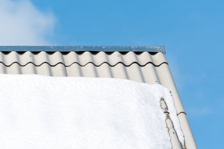 Close up photo of roof is covered with snow against cloudy sky. Roof made of slate or gray metal...