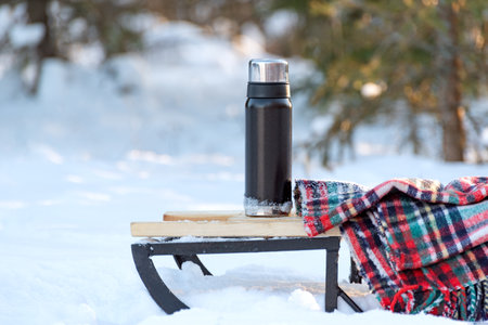 flask and warm woolen blanket on sled in snowy forest. Picnic in winter in forestの写真素材