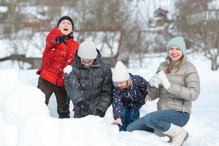 Boys and girls are playing in snowballs. Active outdoors leisure with family with children in winter. Winter holidays.の写真素材
