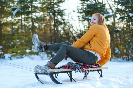 Young woman in yellow jacket rides sled through snow-covered pine forest. Winter holidaysの写真素材