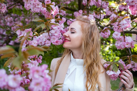 Portrait of happy beautiful woman with wavy hair in blooming park. Attractive smiling girl in white...