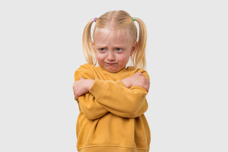 Portrait of sad little girl with blond hair in a yellow sweater. Isolated on white background