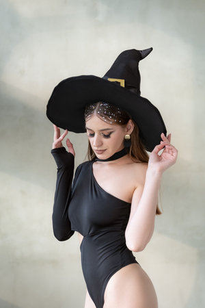 Young beautiful woman in black sexy clothing and witch hat. Closing eyes. Halloween party, sexy...