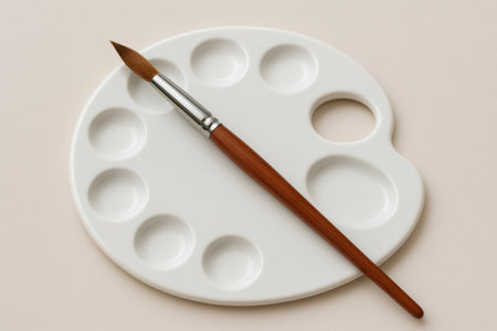 Paintbrush with wooden handle resting on a clean white palette, ready for mixing colors and painting, on a beige backgroundの素材