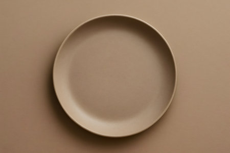 Minimalist image featuring an empty beige ceramic plate on a matching background, ideal for food and lifestyle themesの素材