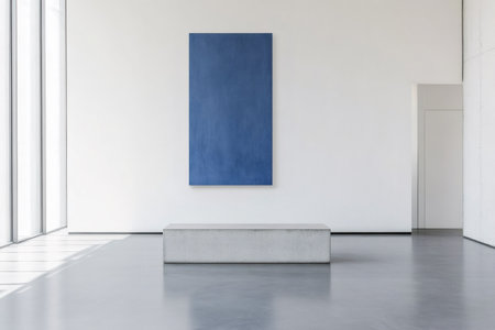 Modern minimalist art gallery with concrete floor and bench exhibiting a blue monochrome painting on a white wallの素材