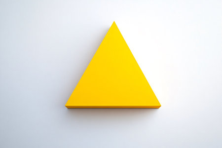 Yellow triangle casting a subtle shadow on a white background, creating a minimalist and geometric compositionの素材