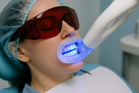 Dentist is using ultraviolet lamp for teeth whitening treatment on female patient in dental clinicの素材
