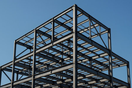 Metal framework of a building under construction, showcasing industrial design and architectural progress against a vibrant blue skyの素材