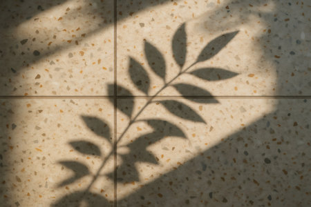 Sunlight casts the shadow of a leaf on a terrazzo tile surface, creating an aesthetically pleasing abstract patternの素材