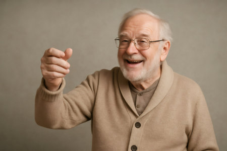 Elderly man with glasses and beige cardigan holding an invisible tiny object between his fingers, smiling and looking awayの素材