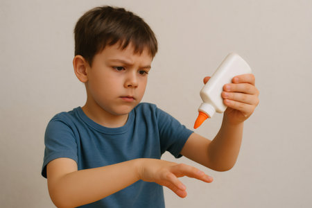 Young boy concentrating while using glue for an art project, demonstrating focus and creativityの素材