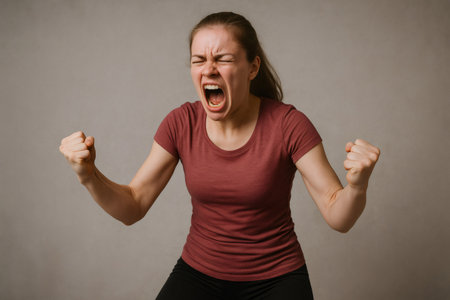 Studio shot of a young woman screaming and raising her fists in a sign of victory, celebrating success and achievementの素材