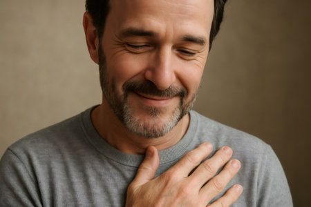 Portrait of a middle aged man with a beard and gray hair, smiling and holding his hand on his chest, expressing gratitude and reliefの素材