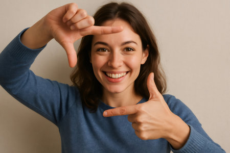 Cheerful young woman framing her face with her fingers, expressing creativity and a positive attitudeの素材
