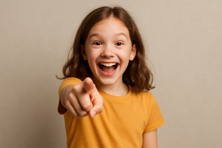 Portrait of a cheerful girl with brown hair wearing an orange t shirt, pointing her finger and laughing out loudの素材