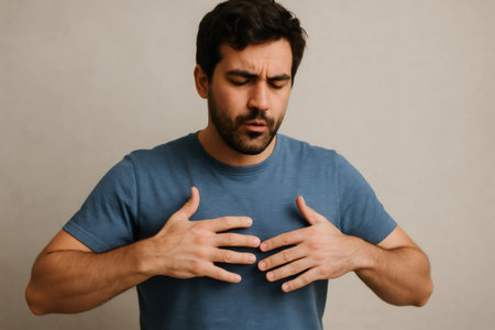 Young man experiencing chest pain, possible heart attack or anxiety, holding his chest with a worried expressionの素材